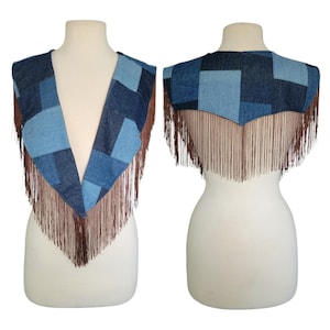 May include: A denim vest with a patchwork design in shades of blue. The vest features long brown fringe along the bottom edge. The vest is displayed on a mannequin.