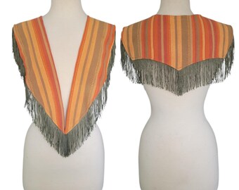 May include: A vintage, fringed shawl displayed on a mannequin. The shawl features vertical stripes in shades of orange, tan, and peach. The bottom edge is trimmed with long, gray fringe. The shawl is shown from the front and back.