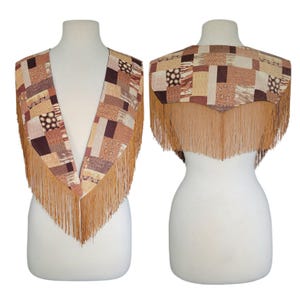 May include: A sleeveless vest featuring a patchwork design of various brown, tan, and cream geometric patterns. The garment has a deep V-neckline in the front and a pointed hemline in the back, with long, thin tan fringe trim along the entire edge.