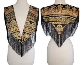 May include: A black vest with a deep V-neckline and a pointed hem, featuring a repeating gold, orange, and blue geometric pattern. The garment is finished with long black fringe trim along the edges, displayed on a mannequin from both front and back.