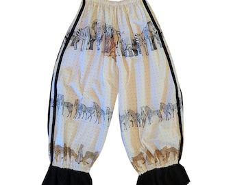 Peut inclure: Pantalon blanc cassé avec un motif répétitif de zèbres, d'éléphants et de léopards. Le vêtement présente une bande verticale noire sur chaque côté, une taille élastique et des poignets noirs à volants avec une bordure en dentelle ajourée.