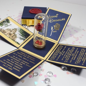 May include: A blue and gold invitation box with a glass dome containing a red rose. The box is open and the invitation card reads "We would like to invite you to be our guests on September 22nd, 2019 for our wedding at  Cernhill Castle, Center Road, Biggar, ML12 6DE."
