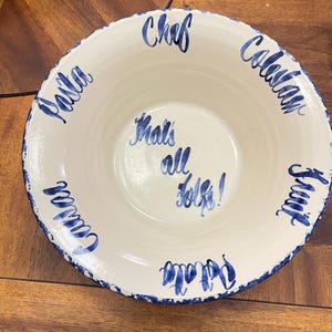 May include: A white ceramic serving bowl with a blue rim and blue lettering. The words "Pasta", "Chef", "Coleslaw", "Fruit", and "Potato" are written around the rim. The phrase "That's all folks!" is in the center.