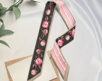May include: A silk scarf with a floral peony design. The scarf features a black background with pink peony flowers and green leaves. The other side has pink and white stripes. The scarf is a stylish accessory.