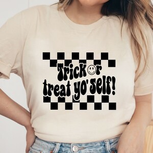May include: A white t-shirt with a black and white checkered pattern and the text "Trick or treat yo' self!" in a retro font.
