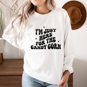 May include: White long-sleeve sweatshirt with black text that reads "I'm just here for the candy corn".