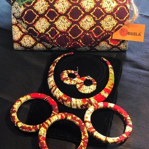 May include: A set of three red, yellow, and green fabric bracelets and a matching necklace. The necklace and bracelets have a geometric pattern. The set is displayed on a black velvet surface.