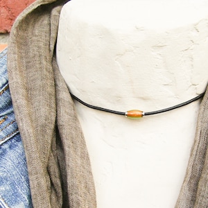 May include: A simple black leather necklace with a single orange and green bead.