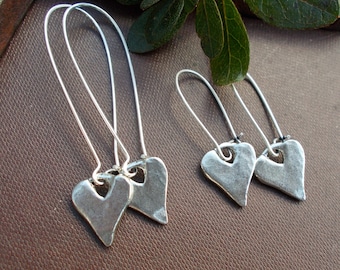 May include: Three pairs of silver dangle earrings with heart-shaped charms. The hearts have a hammered texture and a hole in the center.