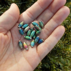 May include: A collection of iridescent oval-shaped beads with silver accents. The beads are a mix of blue, green, and purple colours.
