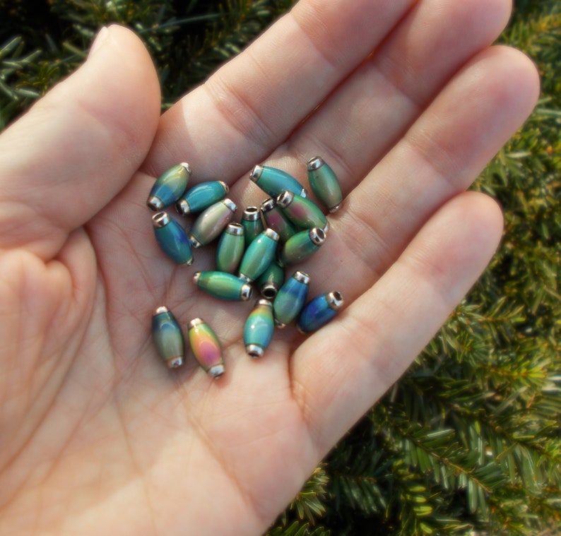 May include: A collection of iridescent oval-shaped beads with silver accents. The beads are a mix of blue, green, and purple colours.
