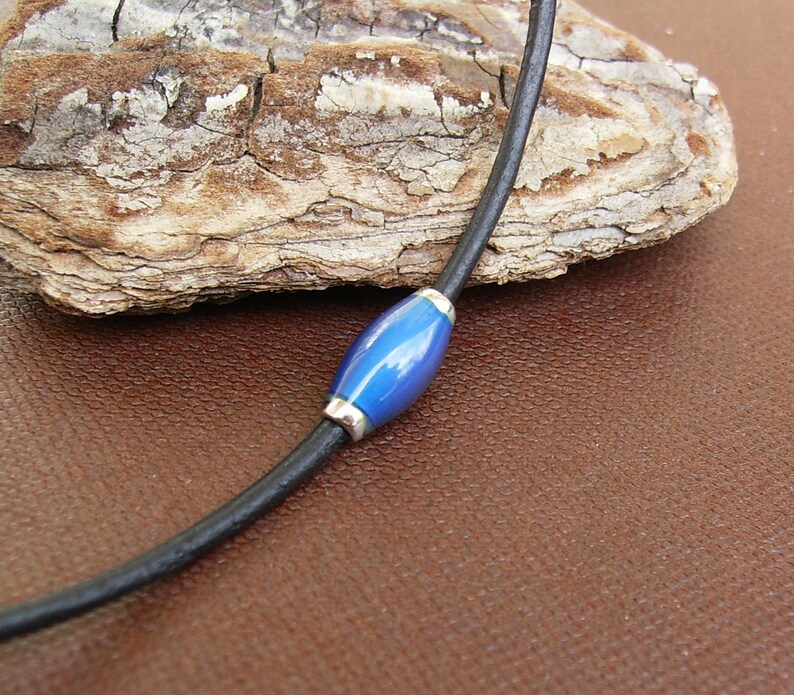 May include: A black leather cord necklace with a single blue glass bead.