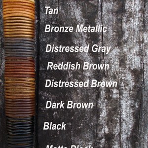 May include: A vertical stack of leather cord samples in various colours and finishes, including pearl metallic, sand, tan, bronze metallic, distressed grey, reddish brown, distressed brown, dark brown, black, matte black, and gunmetal metallic.