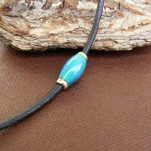 May include: A black leather cord necklace with a single blue and green glass bead.