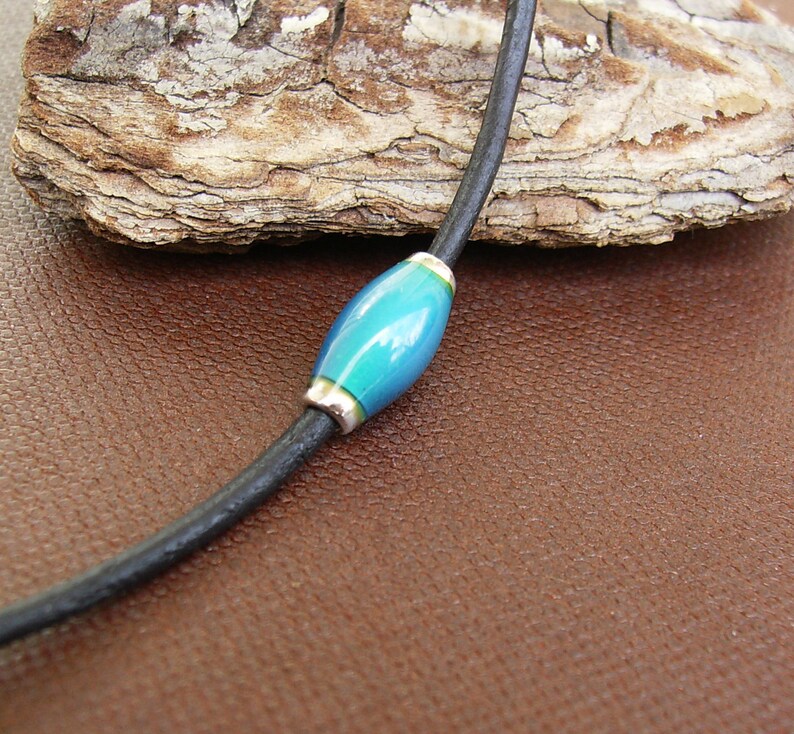May include: A black leather cord necklace with a single blue and green glass bead.