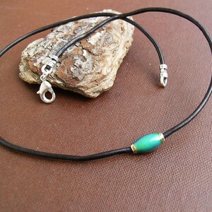 May include: A black leather cord necklace with a silver clasp and a single green oval bead.