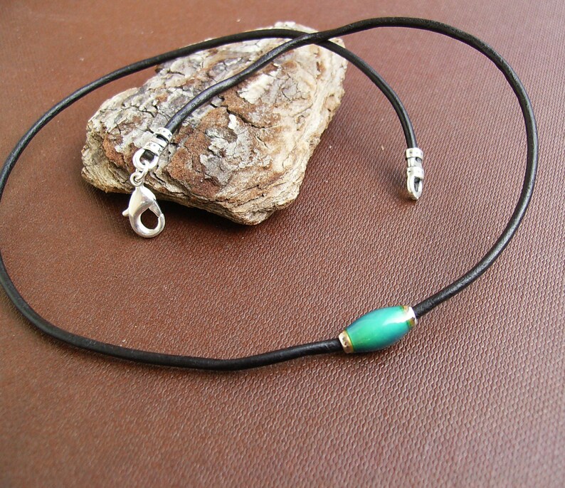 May include: A black leather cord necklace with a silver clasp and a single green oval bead.