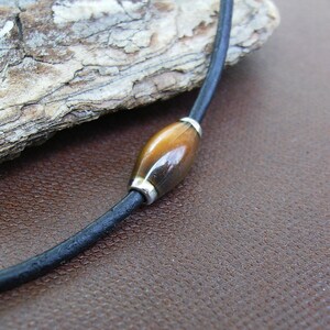 May include: A brown leather cord necklace with a single oval-shaped tiger's eye bead.