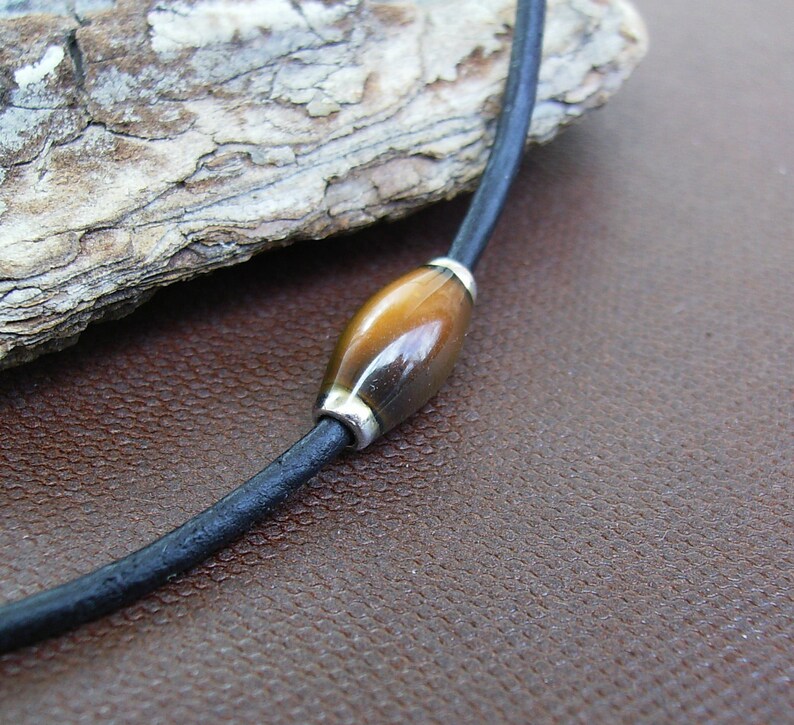 May include: A brown leather cord necklace with a single oval-shaped tiger's eye bead.