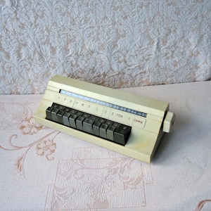 Puede incluir: Una calculadora vintage blanca con teclas negras etiquetadas con números y letras cirílicas. La calculadora tiene una pantalla deslizante con los números del 1 al 3, M, 10, C, 5, B, MOH y una etiqueta SUMMA.