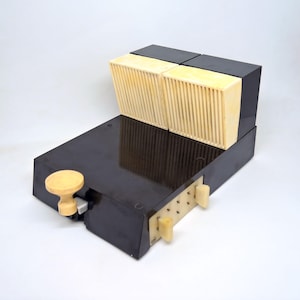 Op de afbeelding: Een vintage radio in zwart en crème met een houten knop en een reeks kleine witte knoppen aan de zijkant.