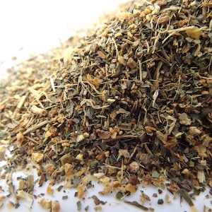 May include: Close-up of a pile of dried herbs and spices. The mix includes green, brown, and tan elements, with visible pieces of leaves, stems, and granules. The texture appears coarse and natural, suggesting a blend for culinary or medicinal use.