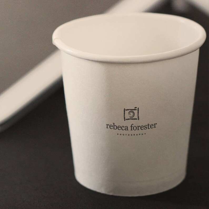 May include: White paper cup with a black and white logo that says "rebecca forester photography" and a camera icon.