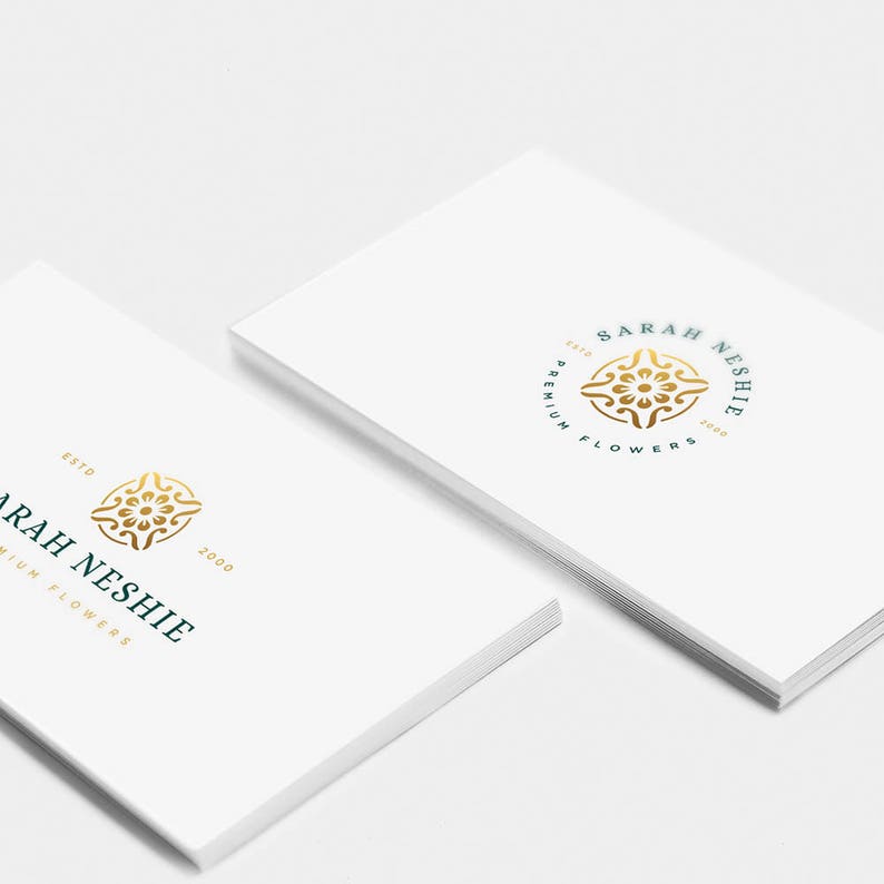 May include: Two white business cards with a gold and teal logo. The logo is a circle with a stylized floral design inside. The text on the card reads "Sarah Neshie Est. 2000 Premium Flowers".