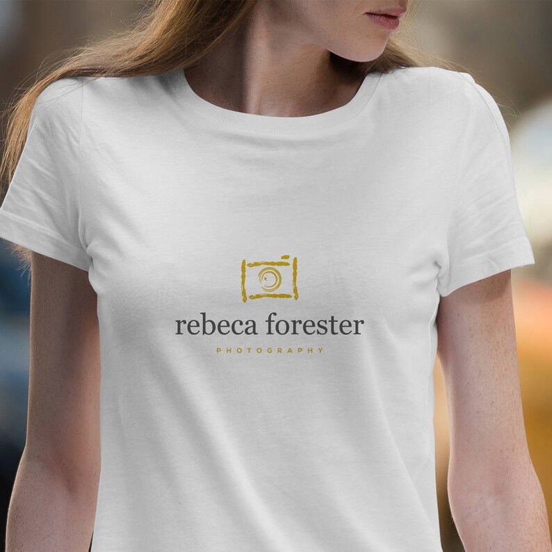 May include: White t-shirt with a gold camera graphic and the text "rebeca forester PHOTOGRAPHY" printed on the front.