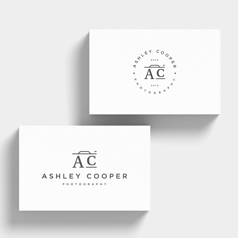 Puede incluir: Dos tarjetas de visita blancas con un logotipo de fotograf&iacute;a minimalista. El logotipo presenta las iniciales "AC" con un icono de c&aacute;mara y el nombre "Ashley Cooper Photography". Una tarjeta tiene un dise&ntilde;o de logotipo circular.