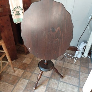 May include: A dark brown, round side table with a scalloped edge. The table has a tripod base with turned legs. The tabletop is approximately 24 inches in diameter. The table is made of wood and has a dark stain.