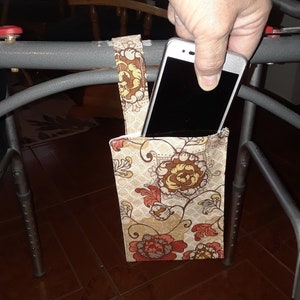 May include: A floral patterned phone holder with a strap, attached to a walker, with a smartphone inside.