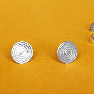 May include: A pair of silver earrings with a circular design featuring a concentric spiral pattern.