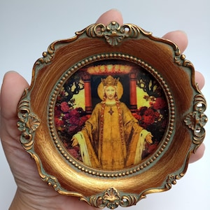 Op de afbeelding: Een goudkleurig ingelijst beeld van een vrouw in een kroon en een gele jurk, staand in een tuin met rode rozen. De lijst heeft een groene patina en sierlijke details.