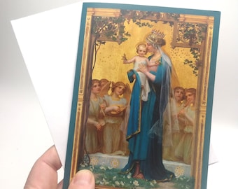 May include: A greeting card featuring a religious illustration. The artwork depicts a woman in a blue robe holding a child, surrounded by angels. The card has a teal border and is held with a white envelope.