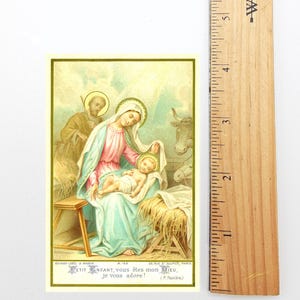 May include: A vintage religious card featuring a depiction of the Nativity scene. The image shows Mary, Joseph, and baby Jesus, with a cow in the background. The card has text in French at the bottom and is framed with a yellow border.