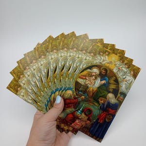Peut inclure: Une collection de cartes de Noël vintage avec des images religieuses. Les cartes représentent la scène de la Nativité avec des anges et la Sainte Famille, disposées en éventail. Les cartes ont un schéma de couleurs or et marron.