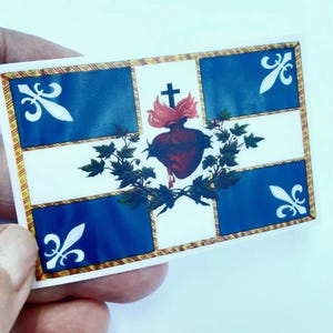 May include: A white flag with a blue cross and a red heart with a crown of thorns and a cross on top. The heart is surrounded by green leaves and the flag has a gold border.