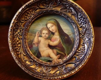 May include: A round, antique-style framed painting featuring a mother and child. The frame is ornate with a gold finish and grape vine detailing. The painting depicts a woman in a dark green veil holding a baby.