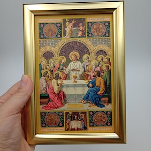 Op de afbeelding: Een religieus kunstwerk met een gouden lijst. Het kunstwerk toont een bijbelse scène met figuren in gewaden, verzameld rond een tafel. De afbeelding heeft een gedetailleerd, kleurrijk ontwerp met tekst aan de boven- en onderkant.