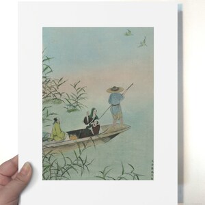 Op de afbeelding: Een ingelijste prent van een traditioneel Japans schilderij met figuren in een boot op een meer. Het kunstwerk heeft zachte kleuren, met een man met een strohoed en anderen in de boot. Riet en vogels zijn ook zichtbaar.