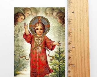 Puede incluir: Una tarjeta religiosa vintage que representa al bebé Jesús con una túnica roja con estrellas doradas, rodeado de ángeles. La tarjeta tiene un halo dorado alrededor de la cabeza de Jesús y el texto "JHS" en su pecho.