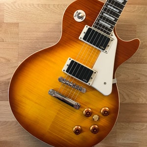 Puede incluir: Una guitarra el&eacute;ctrica con acabado sunburst, herrajes cromados y una golpeador blanco. La guitarra tiene un cuerpo de caoba y una tapa de arce.