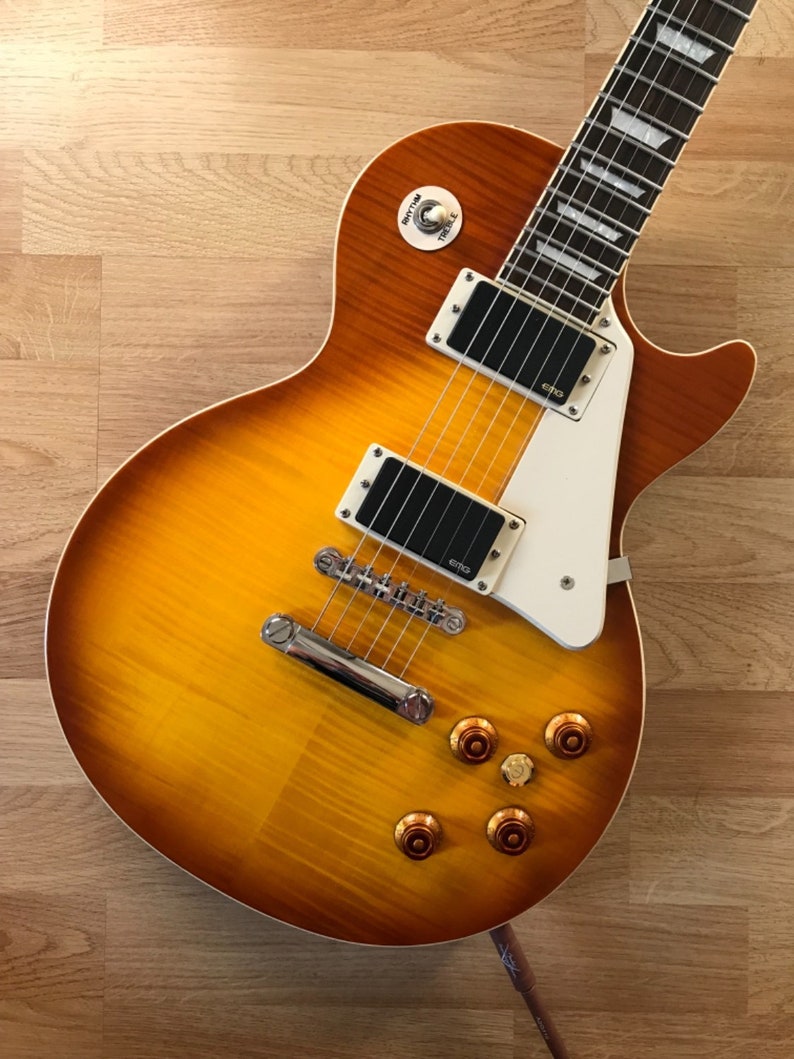 Puede incluir: Una guitarra el&eacute;ctrica con acabado sunburst, herrajes cromados y una golpeador blanco. La guitarra tiene un cuerpo de caoba y una tapa de arce.