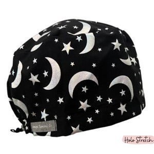May include: Black surgical scrub cap with a pattern of silver crescent moons and stars. The cap is made of a soft fabric and has a tag that reads "Magic Supernova Co." The words "Holo Stretch" are also visible.