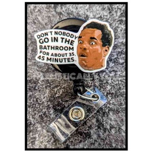 May include: A black retractable badge holder with a white sticker featuring a man's face and the text "Don't nobody go in the bathroom for about 35, 45 minutes."