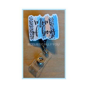 May include: A black retractable badge holder with a blue, peach, and gray patterned rectangle that says "Mom of Boys".