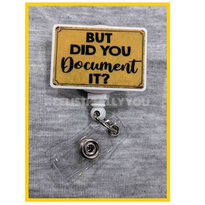 May include: A white retractable badge holder with a yellow and brown sign that reads "But did you document it?"