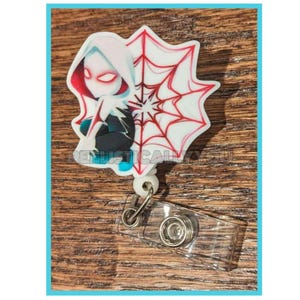 May include: A white and red Spider-Gwen badge reel with a clear plastic clip. The badge reel features a cartoon illustration of Spider-Gwen with a spiderweb design. The text "RENUSTICALY YOU" is visible on the badge reel.
