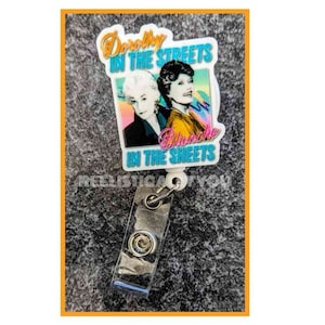 May include: A white plastic badge reel with a colorful image of two women and the text "Dorothy in the Streets Blanche in the Sheets".